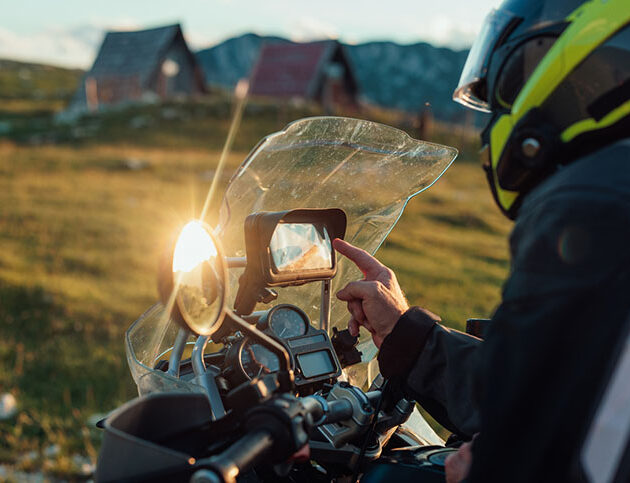 A man on the motorcycle looks at the directions from the navigation Biker with safety helmet searching global positioning system on smart phone